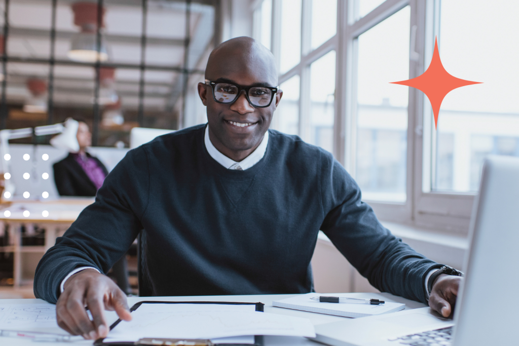 Confident professional smiling at his desk with laptop and documents, ready to tackle the call support for franchises workday.